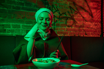 Image showing Beautiful girl with a pearl earring taking lunch in modern cafe, restaurant in neon light