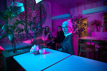 Image showing Beautiful girl with a pearl earring taking lunch in modern cafe, restaurant in neon light