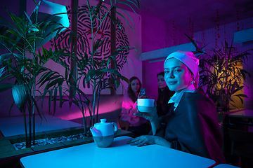 Image showing Beautiful girl with a pearl earring taking lunch in modern cafe, restaurant in neon light