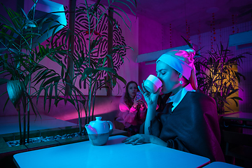 Image showing Beautiful girl with a pearl earring taking lunch in modern cafe, restaurant in neon light