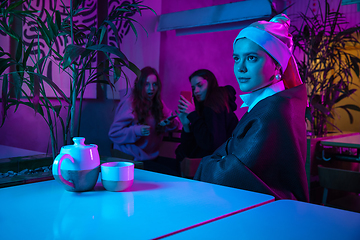 Image showing Beautiful girl with a pearl earring taking lunch in modern cafe, restaurant in neon light