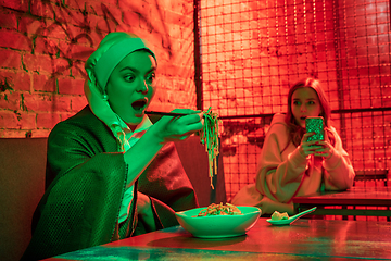 Image showing Beautiful girl with a pearl earring taking lunch in modern cafe, restaurant in neon light