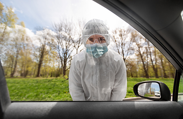 Image showing healthcare worker in hazmat suit looking into car