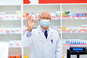 Image showing senior apothecary in mask at pharmacy showing ok