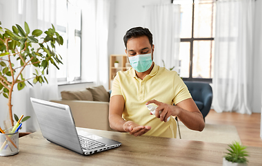 Image showing man in mask using hand sanitizer at home office