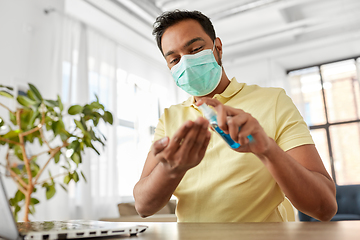 Image showing man in mask using hand sanitizer at home office