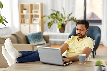 Image showing man with laptop resting feet on table at home