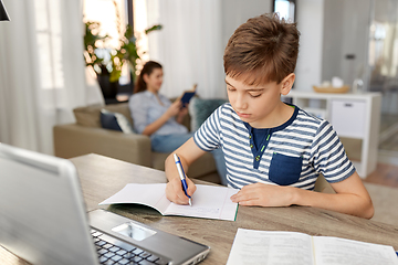 Image showing student boy with book writing to notebook at home