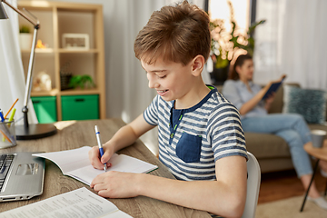 Image showing student boy with book writing to notebook at home