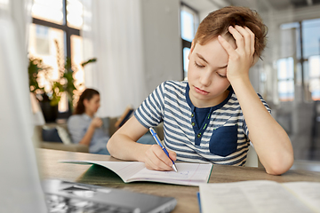 Image showing student boy with book writing to notebook at home