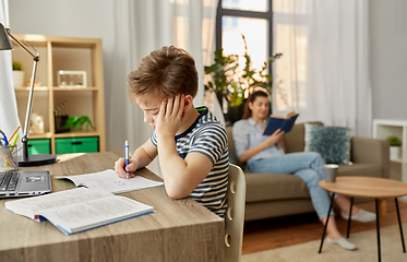 Image showing student boy with book writing to notebook at home