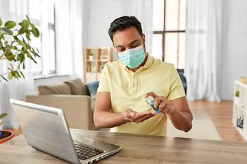 Image showing man in mask using hand sanitizer at home office