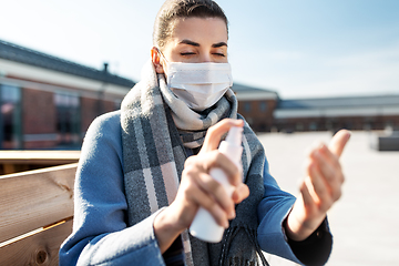 Image showing woman in mask spraying hand sanitizer outdoors