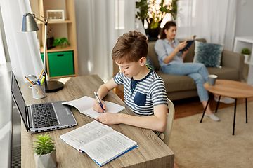 Image showing student boy with book writing to notebook at home