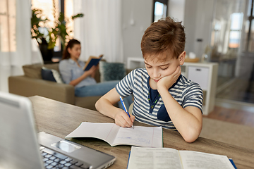 Image showing student boy with book writing to notebook at home