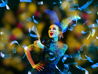 Image showing Beautiful young woman in carnival and masquerade costume in colorful neon lights on black background in flying confetti