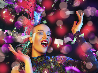 Image showing Beautiful young woman in carnival and masquerade costume in colorful neon lights on black background in flying confetti