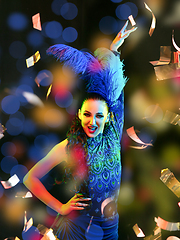 Image showing Beautiful young woman in carnival and masquerade costume in colorful neon lights on black background in flying confetti