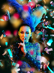 Image showing Beautiful young woman in carnival and masquerade costume in colorful neon lights on black background in flying confetti