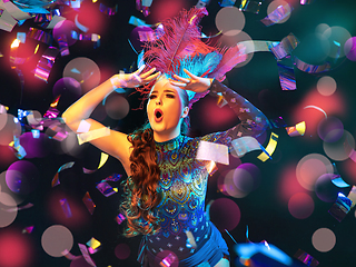 Image showing Beautiful young woman in carnival and masquerade costume in colorful neon lights on black background in flying confetti