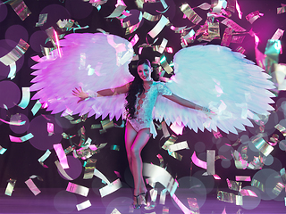 Image showing Young female dancer with angel\'s wings in neon light on black background in flying confetti