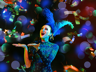 Image showing Beautiful young woman in carnival and masquerade costume in colorful neon lights on black background in flying confetti