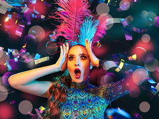 Image showing Beautiful young woman in carnival and masquerade costume in colorful neon lights on black background in flying confetti
