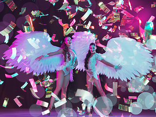 Image showing Young female dancers with angel\'s wings in neon light on black background in flying confetti