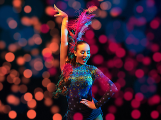 Image showing Beautiful young woman in carnival and masquerade costume in colorful neon lights on black background in flying confetti