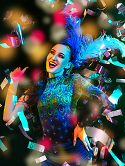 Image showing Beautiful young woman in carnival and masquerade costume in colorful neon lights on black background in flying confetti