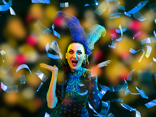 Image showing Beautiful young woman in carnival and masquerade costume in colorful neon lights on black background in flying confetti