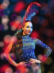 Image showing Beautiful young woman in carnival and masquerade costume in colorful neon lights on black background in flying confetti