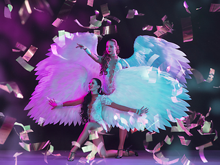 Image showing Young female dancers with angel\'s wings in neon light on black background in flying confetti