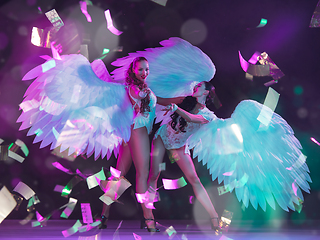 Image showing Young female dancers with angel\'s wings in neon light on black background in flying confetti