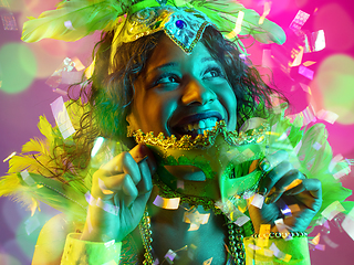 Image showing Beautiful young woman in carnival and masquerade costume in colorful neon lights on gradient background in flying confetti