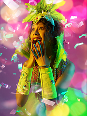 Image showing Beautiful young woman in carnival and masquerade costume in colorful neon lights on gradient background in flying confetti