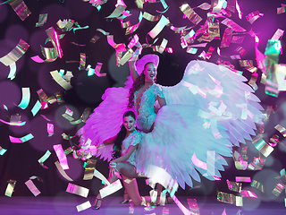 Image showing Young female dancers with angel\'s wings in neon light on black background in flying confetti