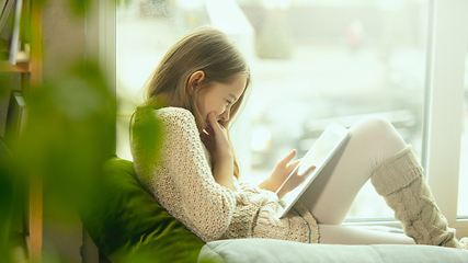 Image showing Little girl sitting near by window with tablet, remote studying, being at home