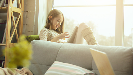 Image showing Little girl sitting near by window with tablet, remote studying, being at home