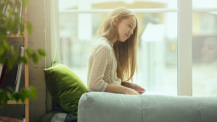 Image showing Little girl sitting near by window with tablet, remote studying, being at home