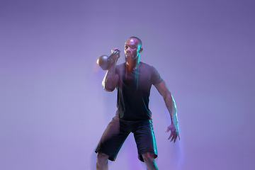 Image showing Young african-american bodybuilder training over purple background in neon, mixed light