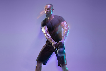 Image showing Young african-american bodybuilder training over purple background in neon, mixed light