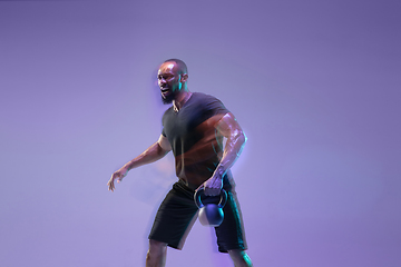 Image showing Young african-american bodybuilder training over purple background in neon, mixed light