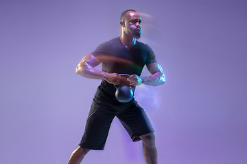 Image showing Young african-american bodybuilder training over purple background in neon, mixed light