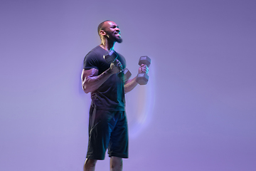 Image showing Young african-american bodybuilder training over purple background in neon, mixed light