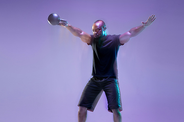 Image showing Young african-american bodybuilder training over purple background in neon, mixed light