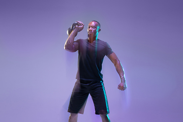 Image showing Young african-american bodybuilder training over purple background in neon, mixed light