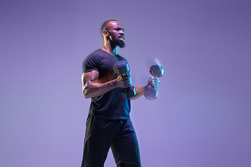 Image showing Young african-american bodybuilder training over purple background in neon, mixed light