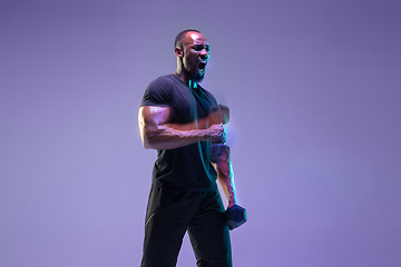 Image showing Young african-american bodybuilder training over purple background in neon, mixed light