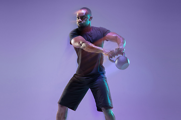 Image showing Young african-american bodybuilder training over purple background in neon, mixed light